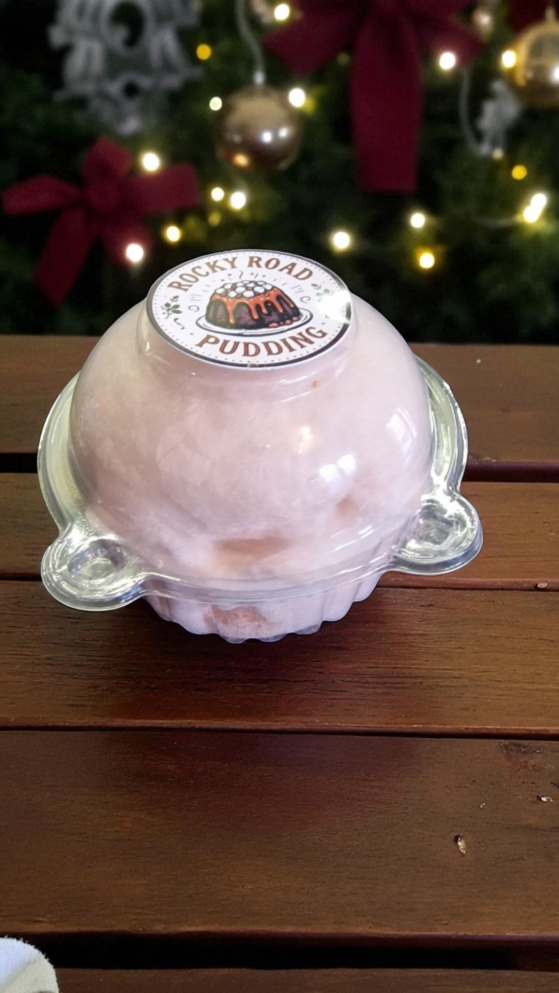 Pink pudding in a clear container with a Rocky Road Puddings label, set against a festive background.