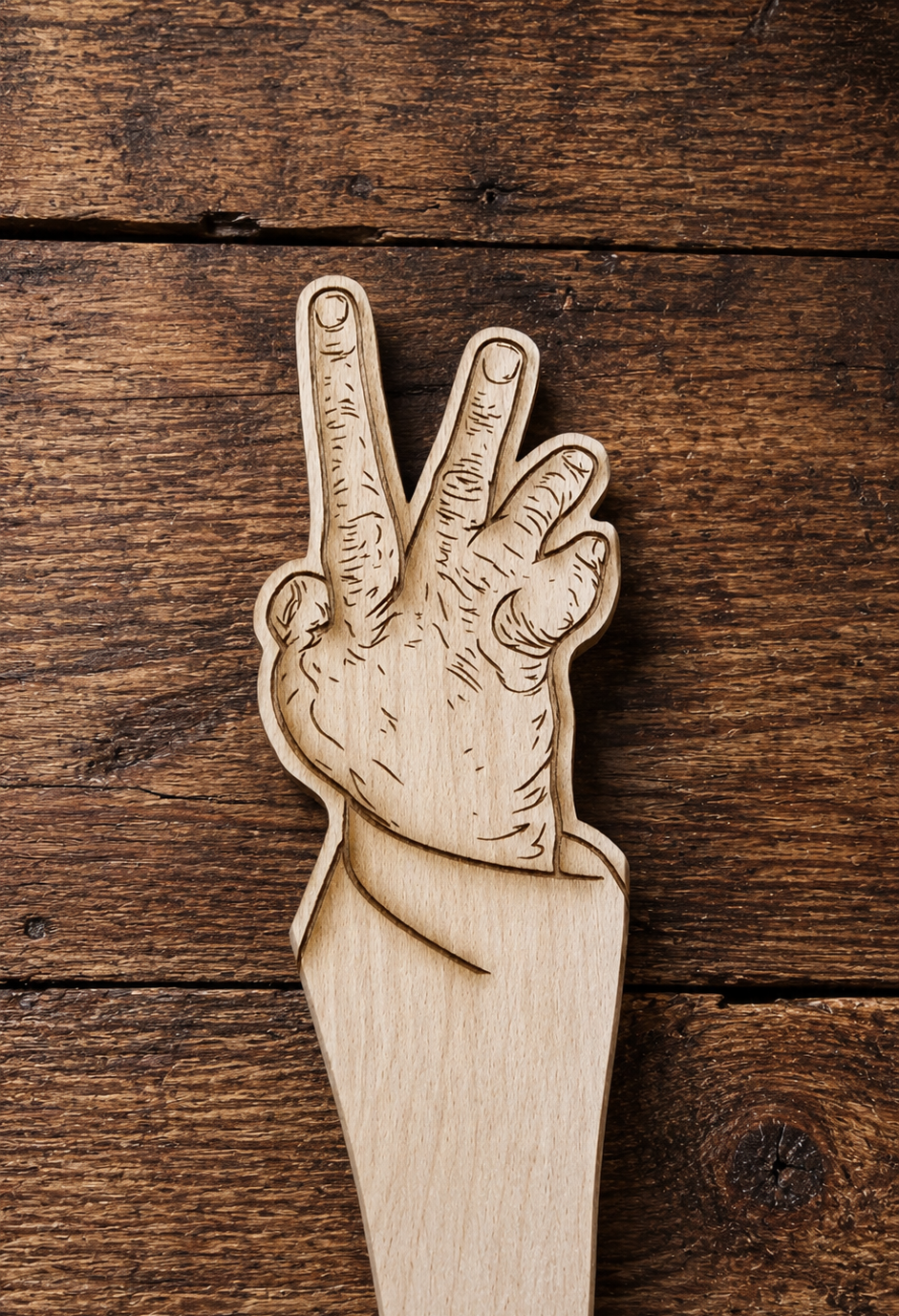 A wooden cutout shaped like a hand making a peace sign, photographed from above on a rustic dark wood plank surface.