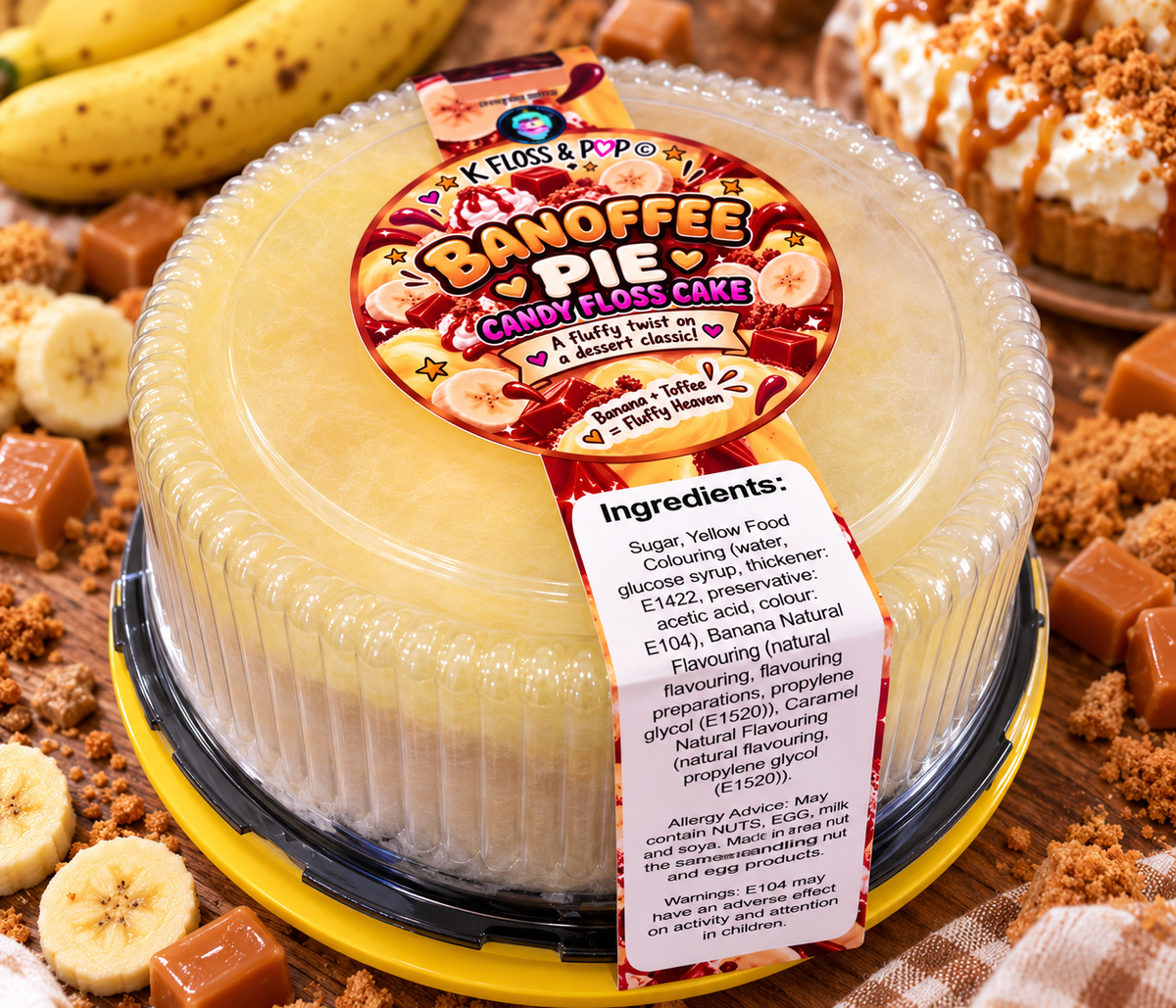 A round plastic tub of Banoffee Pie Candy Cakes by Flossal & Pop, surrounded by banana slices, caramel pieces, and a chocolate cake in the background.