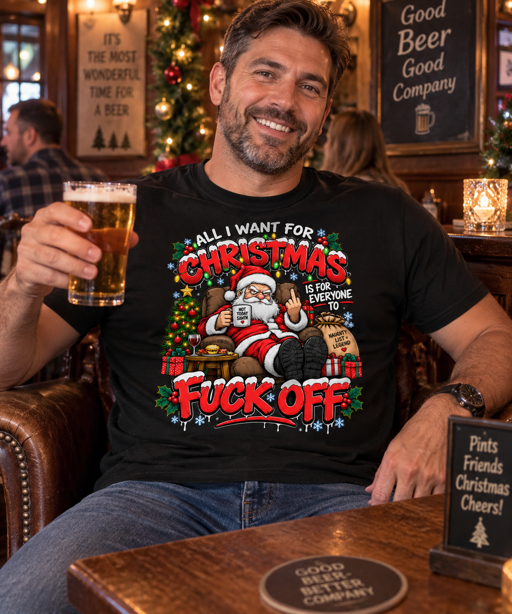 A man sitting in a pub holding a pint of beer, wearing a black graphic t-shirt with a colorful Christmas Santa design and the text 'ALL I WANT FOR CHRISTMAS IS FOR EVERYONE TO FUCK OFF'.
