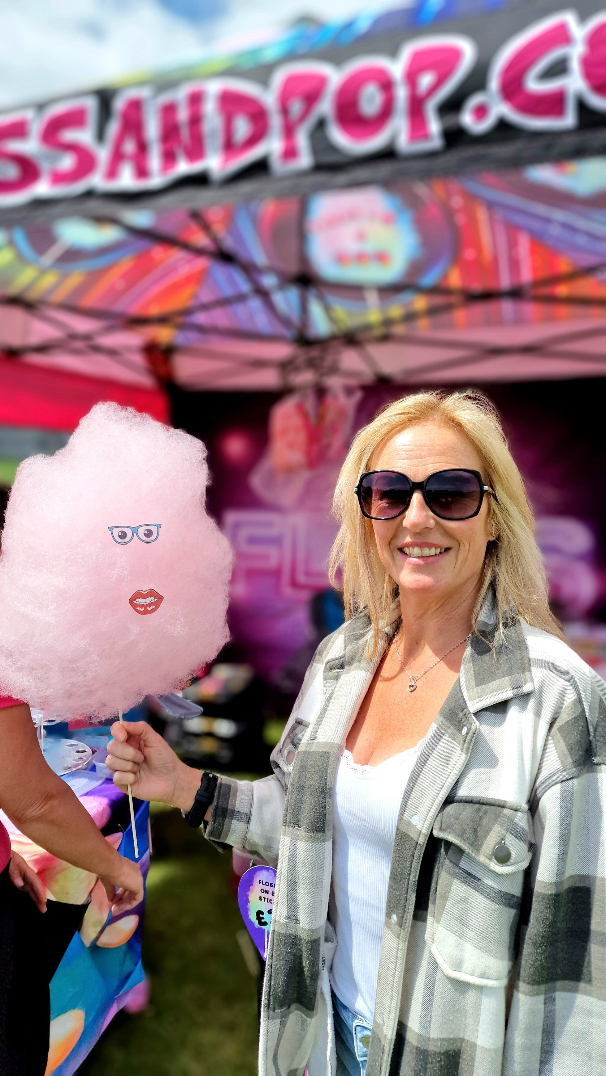 Woman holding pink cotton candy with a face design, standing under a colorful canopy with 'Candy and Pop' branding.