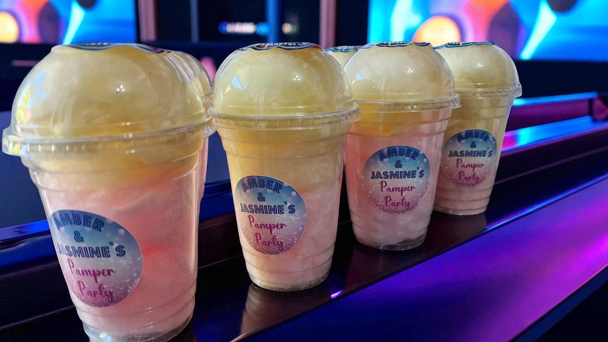 Four colorful drinks in plastic cups with visible branding on a reflective surface.