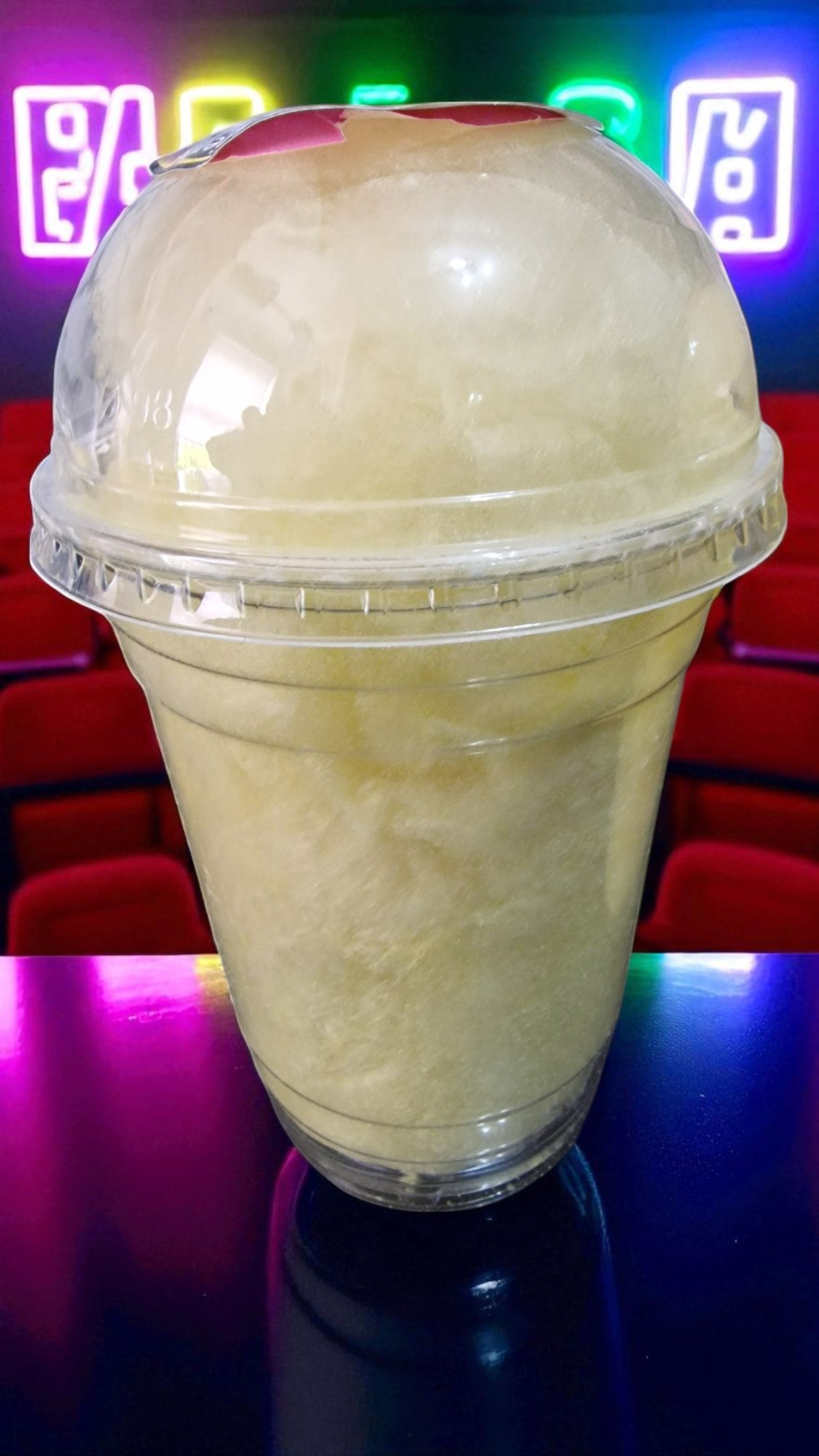 Clear plastic cup with a white liquid on a dark surface with colorful lights in the background