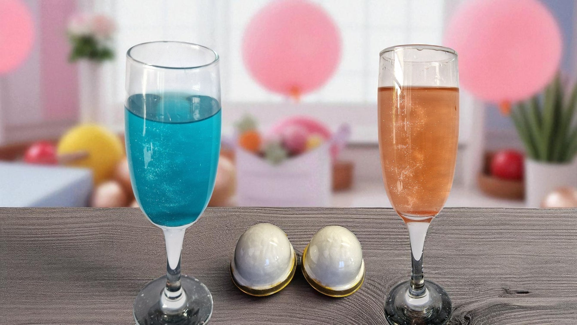 Two glasses of sparkling drinks—one blue, one pink—on a table with two white shimmer candy floss drink bombs in gold domes, perfect for gender reveal parties
