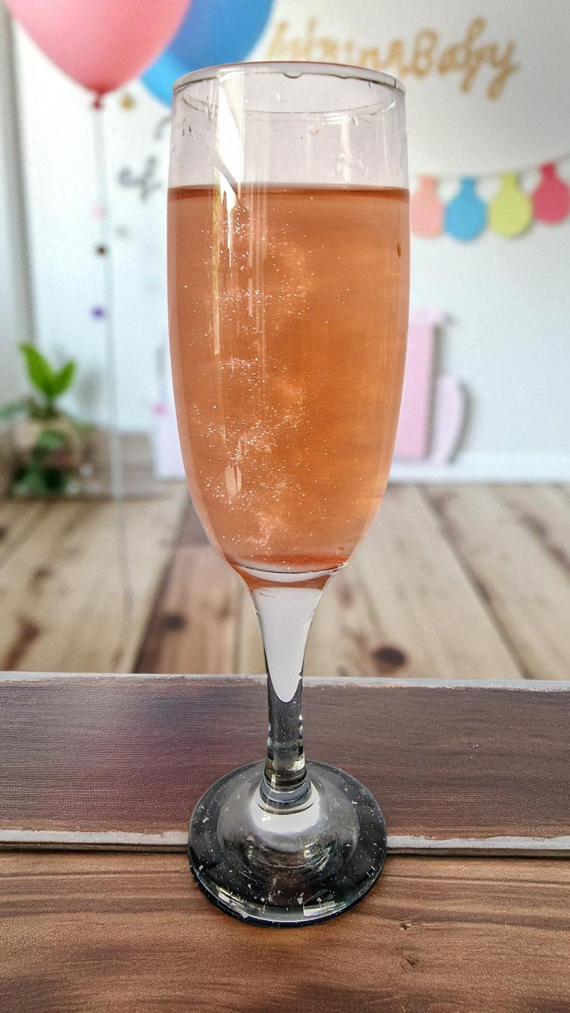 Two glasses of sparkling drinks—one blue, one pink—on a table with two white shimmer candy floss drink bombs in gold domes, perfect for gender reveal parties