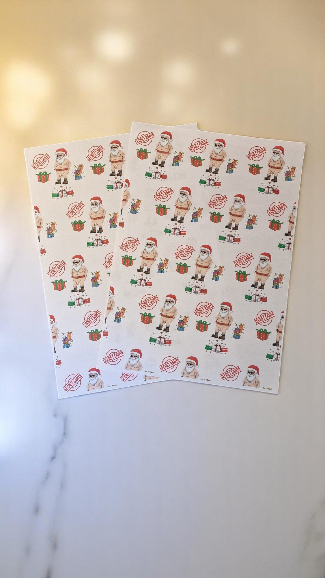 Cheeky Secret Santa Christmas wrapping paper featuring a cartoon naked Santa with gifts, Secret Santa stamps, and colourful presents on white A3 sheets