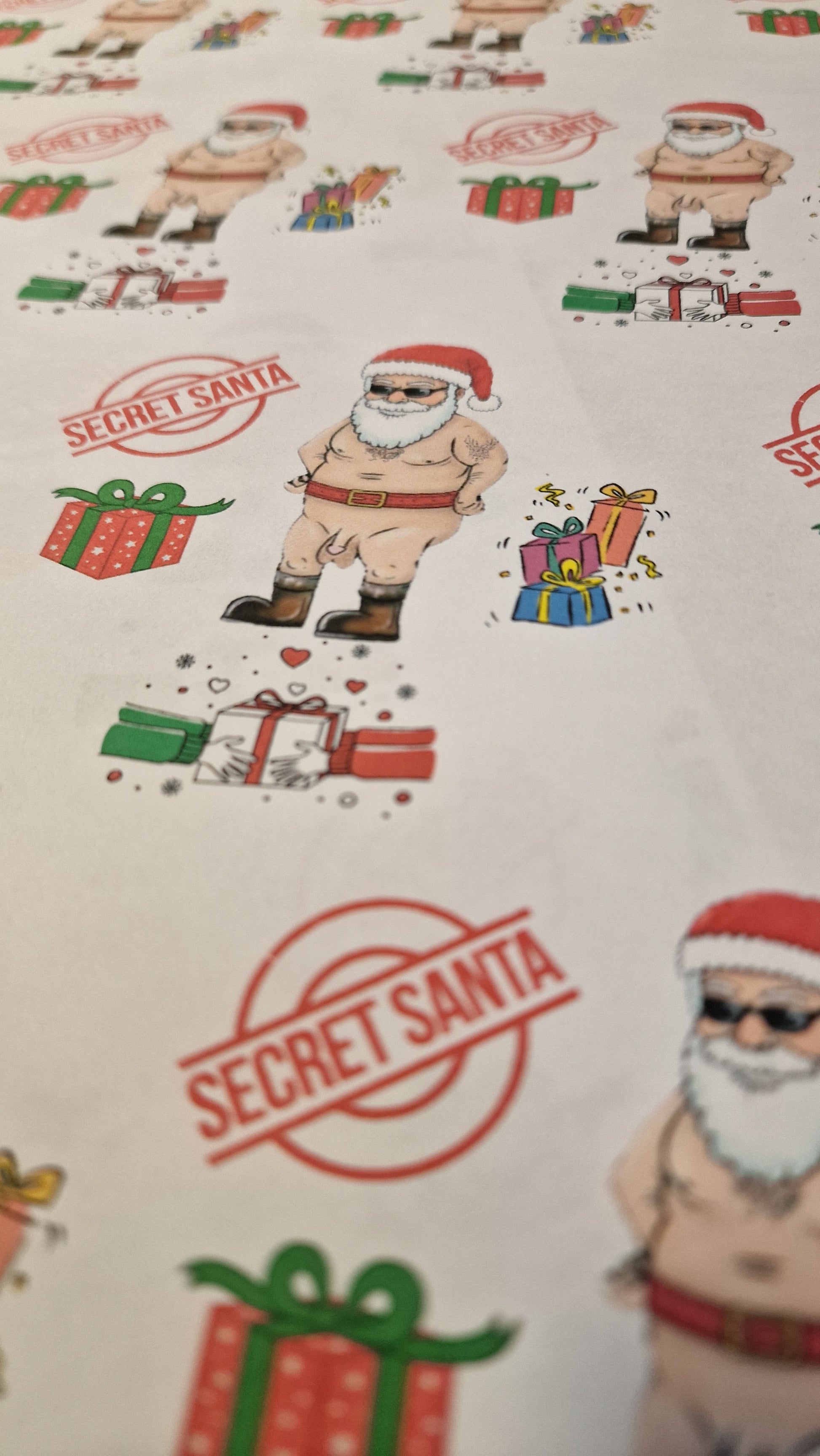 Cheeky Secret Santa Christmas wrapping paper featuring a cartoon naked Santa with gifts, Secret Santa stamps, and colourful presents on white A3 sheets