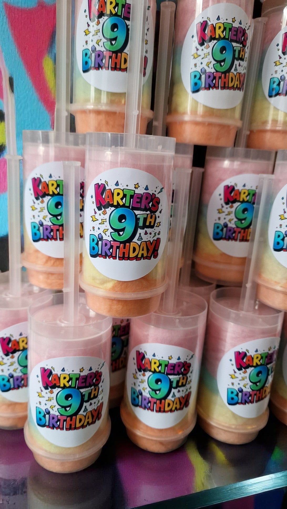 Ten personalised candy floss push pops in clear tubes with custom labels, displayed on a party table with colourful decorations—perfect for kids or adults