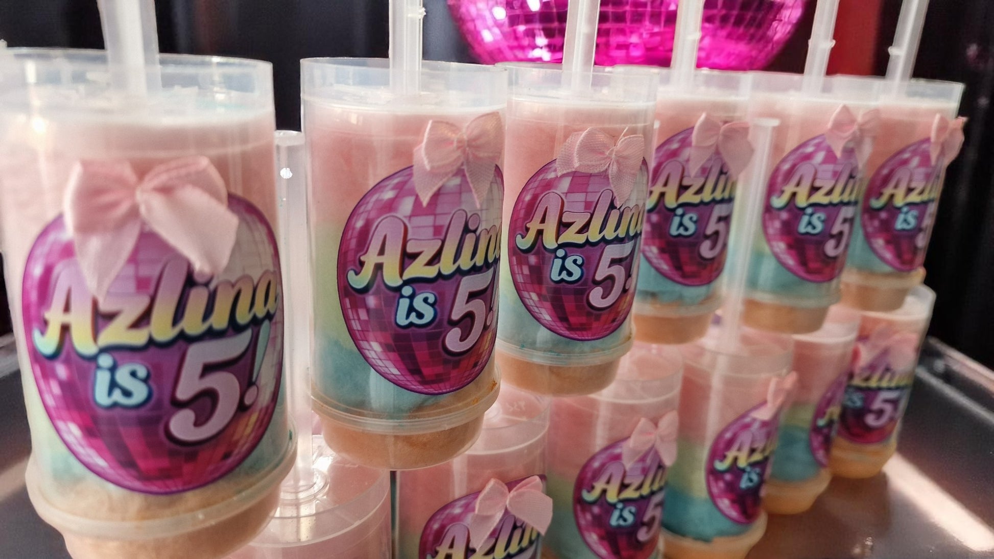 Ten personalised candy floss push pops in clear tubes with custom labels, displayed on a party table with colourful decorations—perfect for kids or adults