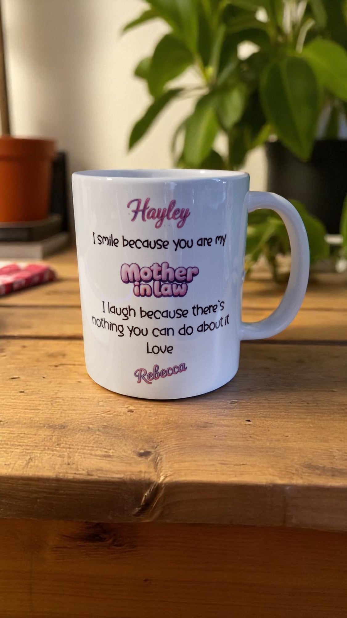 White mug with personalized text on a wooden surface with a plant in the background