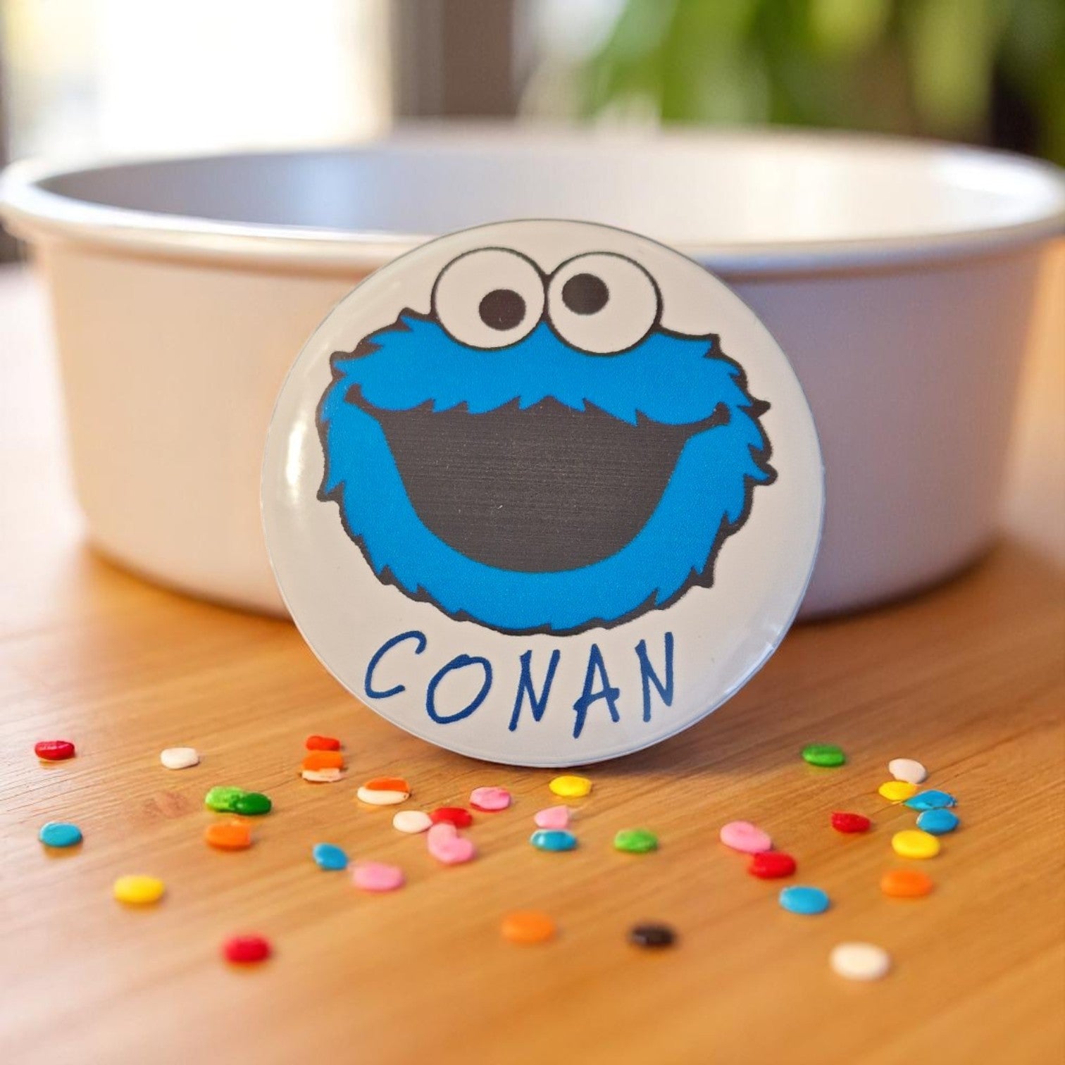 Button with Cookie Monster face and 'CONAN' text on a wooden surface with colorful buttons.
