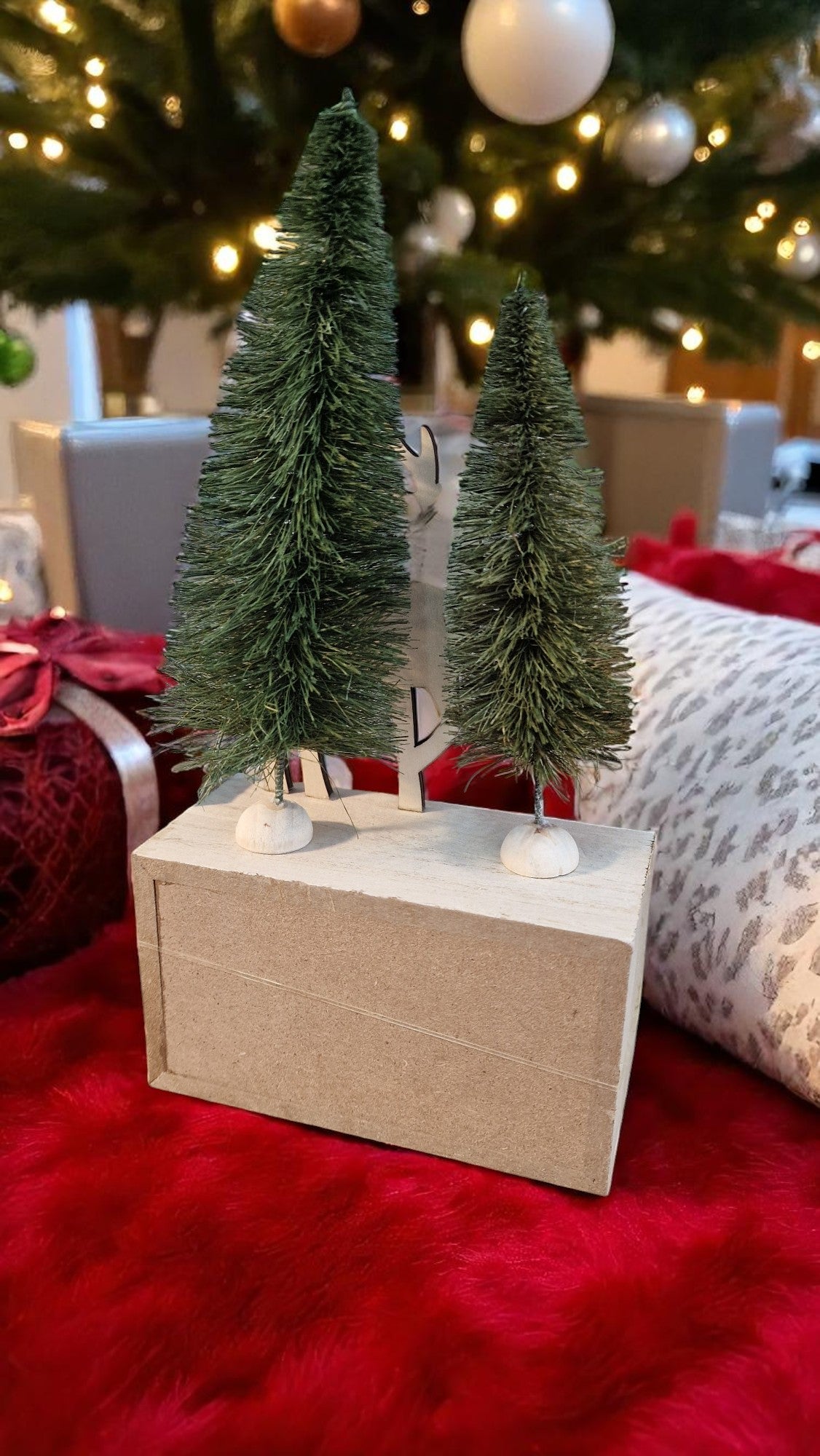Two small Christmas trees on a wooden stand with a festive background.