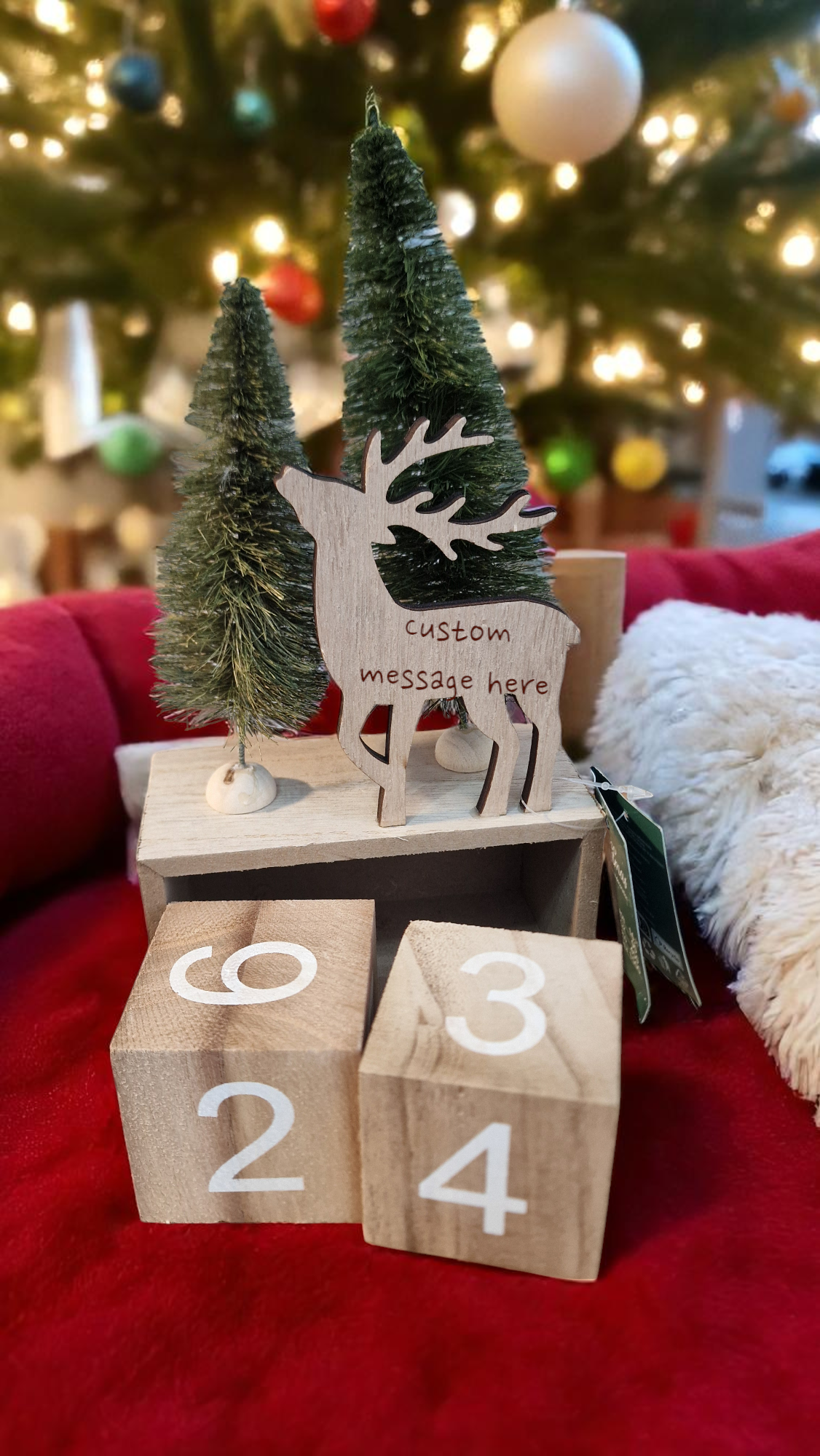 Wooden reindeer figure with custom message on blocks in front of a Christmas tree.