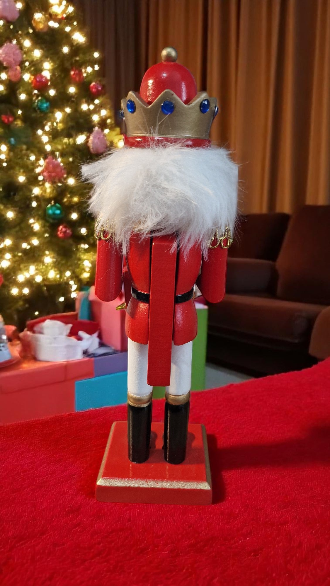 Red and gold wooden nutcracker advent calendar with white beard and hair, holding a gold staff, standing in front of a Christmas tree and gifts, displaying “25 days ‘til Christmas” on countdown blocks.