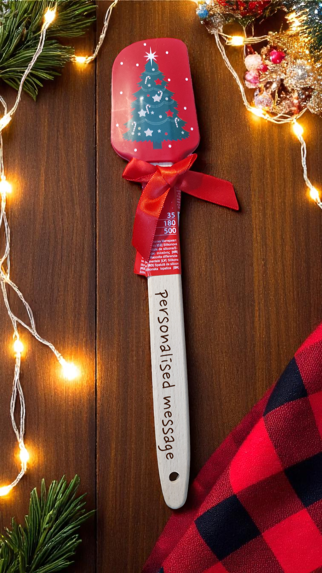Red and white Christmas silicone spatula personalised with a name, surrounded by festive cookies and holiday decorations.