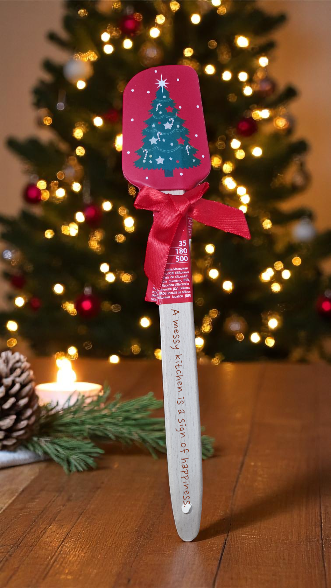 Red and white Christmas silicone spatula personalised with a name, surrounded by festive cookies and holiday decorations.