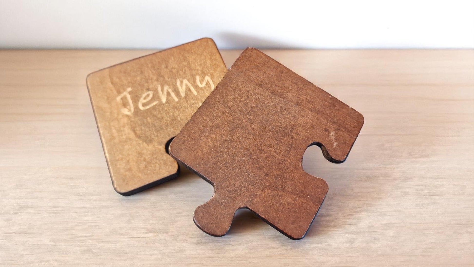 Set of two personalized jigsaw-style wooden coasters, 8x8 cm each, engraved with custom names and a heart design.