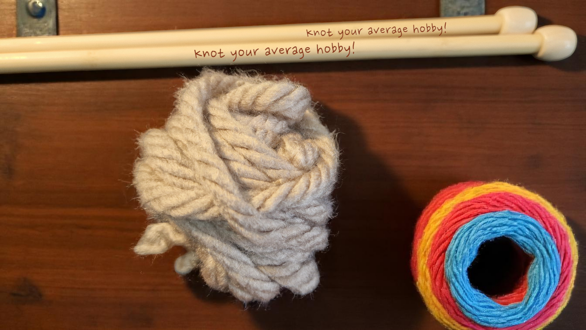 Pair of personalised bamboo knitting needles with engraved messages, chunky wool wrapped around, displayed on a wooden table with colourful yarn in the background