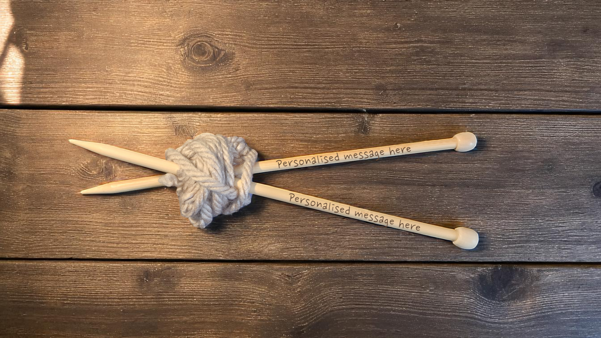 Pair of personalised bamboo knitting needles with engraved messages, chunky wool wrapped around, displayed on a wooden table with colourful yarn in the background