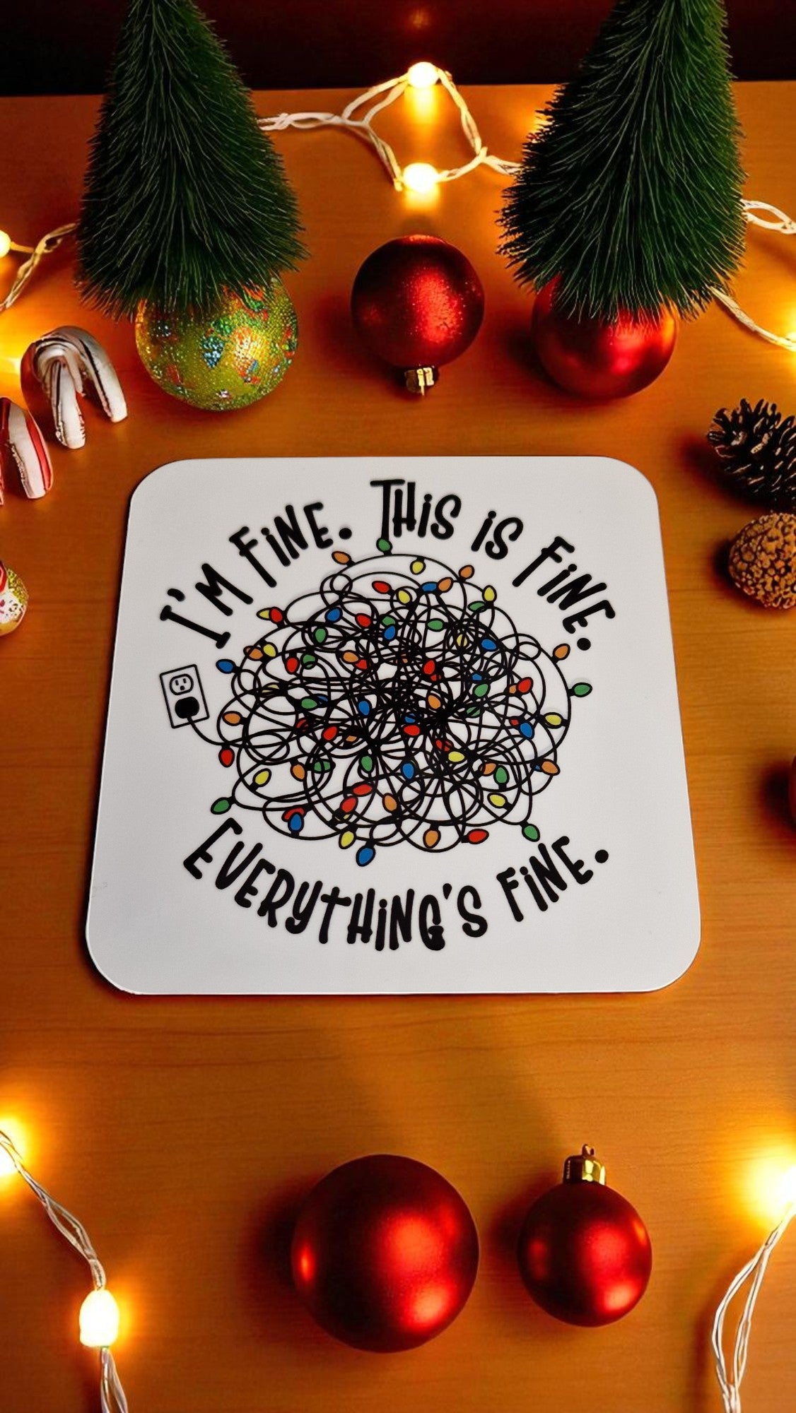 Coaster with 'I'm fine. This is fine. Everything's fine.' text on a wooden surface with Christmas decorations.