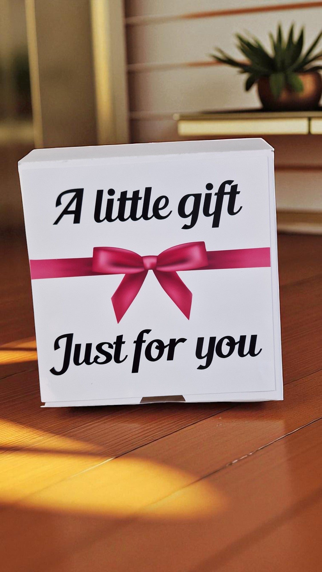 White box with a pink bow and text 'A little gift Just for you' on a wooden surface.