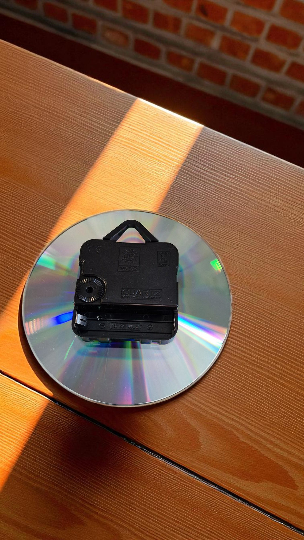 Small black camera on a reflective CD on a wooden surface with a brick wall background
