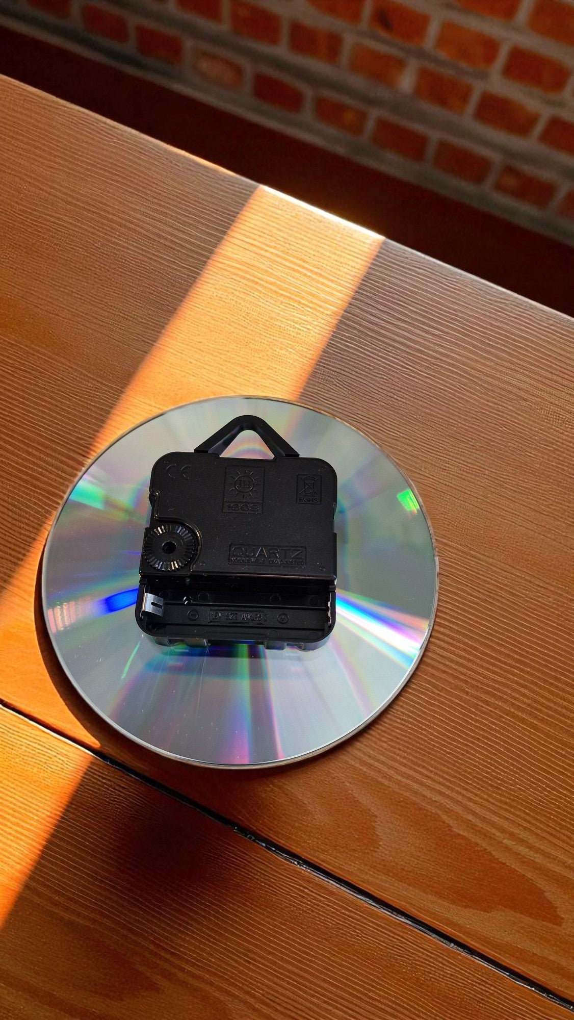 Small black camera on a reflective CD on a wooden surface with a brick wall background