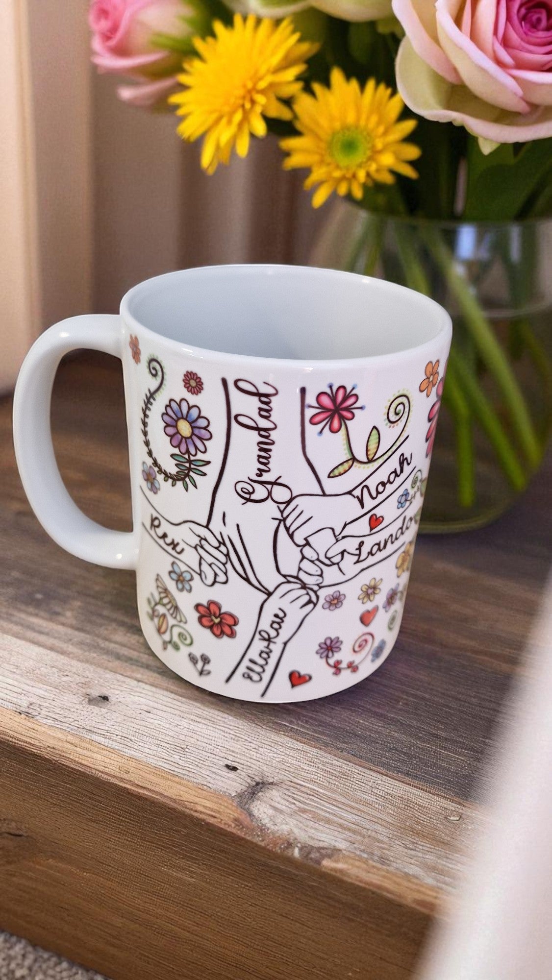 Decorative mug with floral and heart designs on a wooden surface with flowers in the background