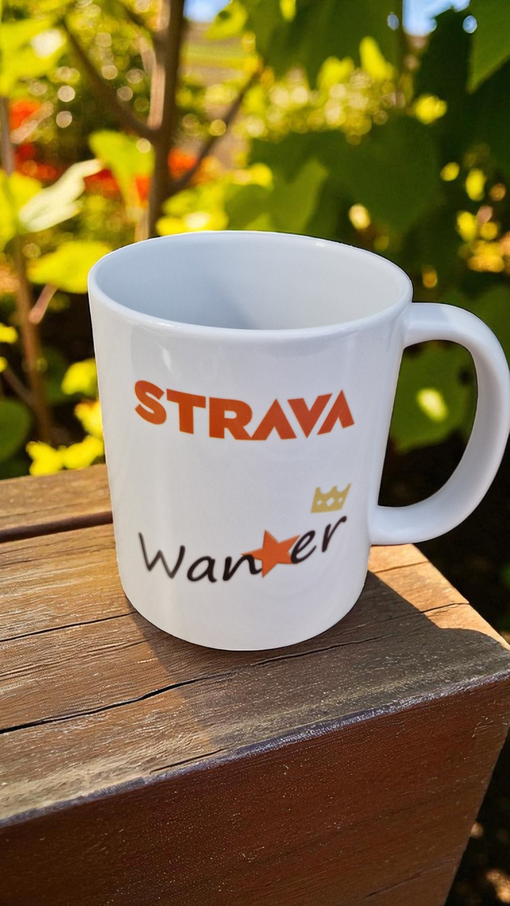 White mug with 'Strava' and 'Wander' text on a wooden surface with greenery in the background