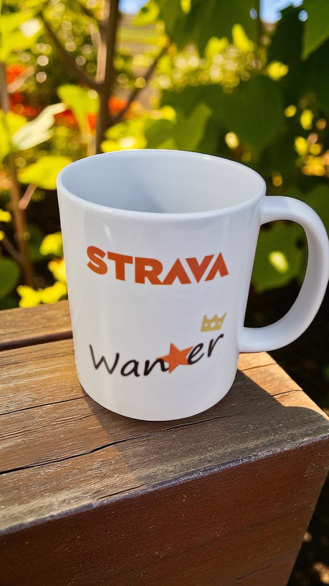 White mug with 'Strava' and 'Wander' text on a wooden surface with greenery in the background