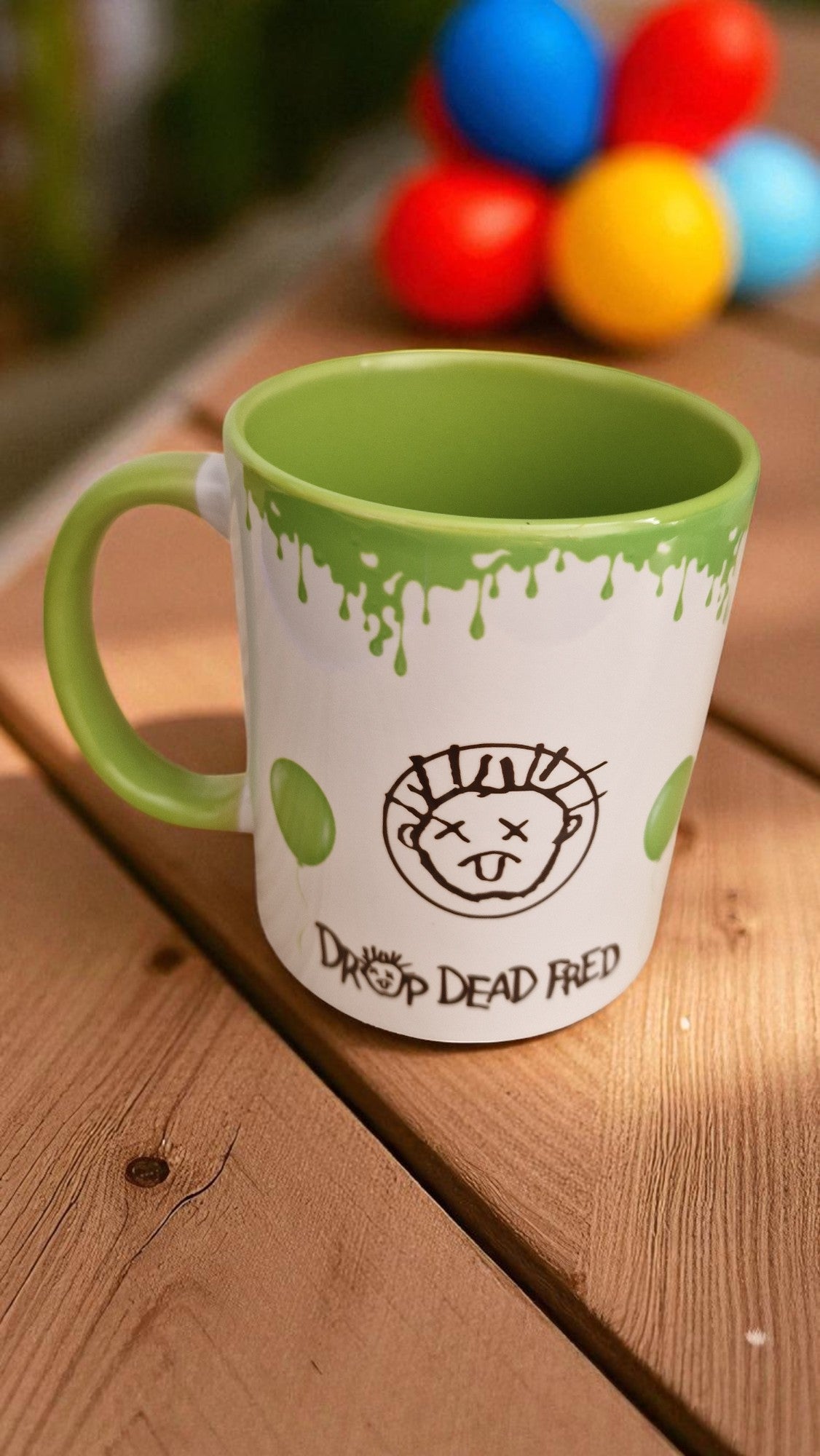 Green mug with a logo and text on a wooden surface with colorful balls in the background
