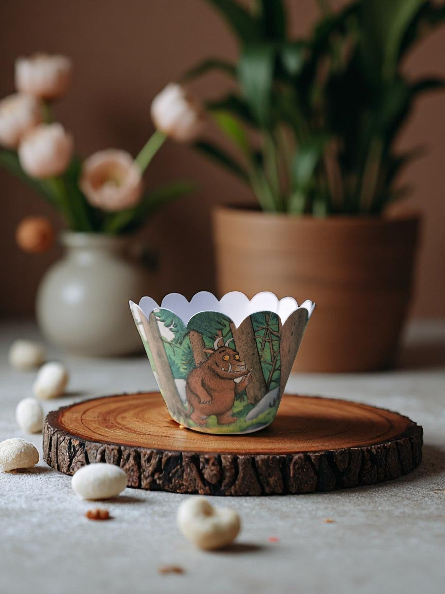 Gruffalo-themed cupcake case wrapper made of cardstock, featuring a colorful forest background with the Gruffalo character in the center, shown flat and unassembled on a wooden surface.