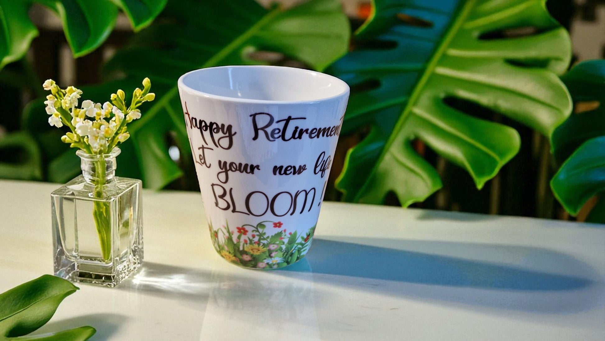 Ceramic mug with floral design and text on a table with green leaves in the background