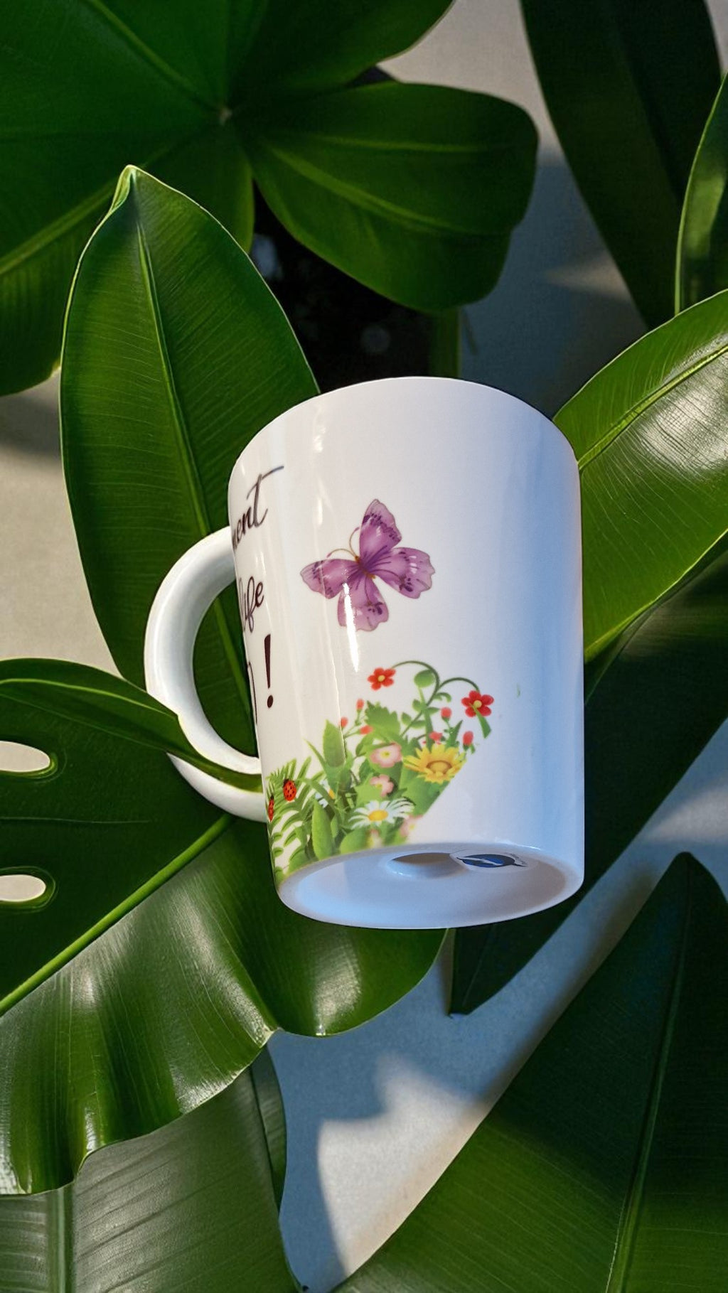 White mug with floral design and butterfly on green leaves
