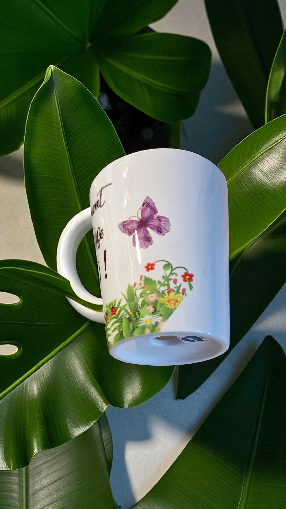 White mug with floral design and butterfly on green leaves