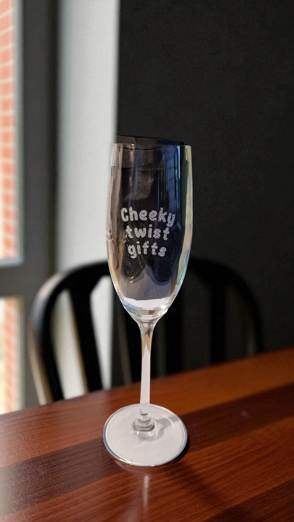 Personalised champagne flute glass engraved with ‘Cheeky twist gifts’, filled with rosé, on a marble kitchen counter with grapes and a bottle in the background