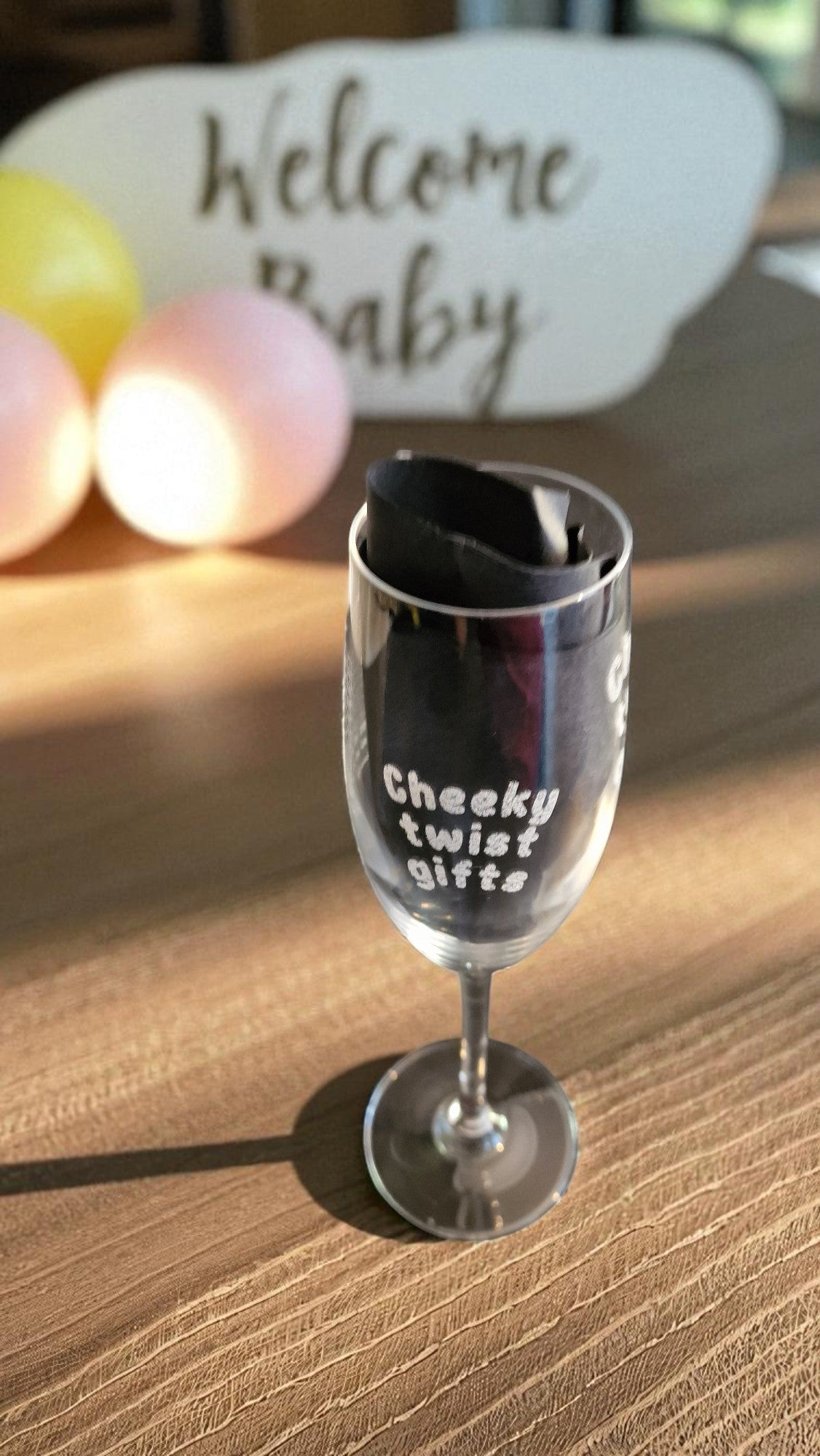 Personalised champagne flute glass engraved with ‘Cheeky twist gifts’, filled with rosé, on a marble kitchen counter with grapes and a bottle in the background