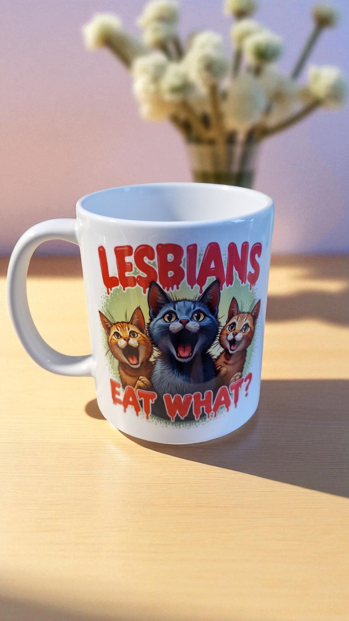 Mug with cartoon cats and text 'LESBIANS EAT WHAT?' on a wooden surface.