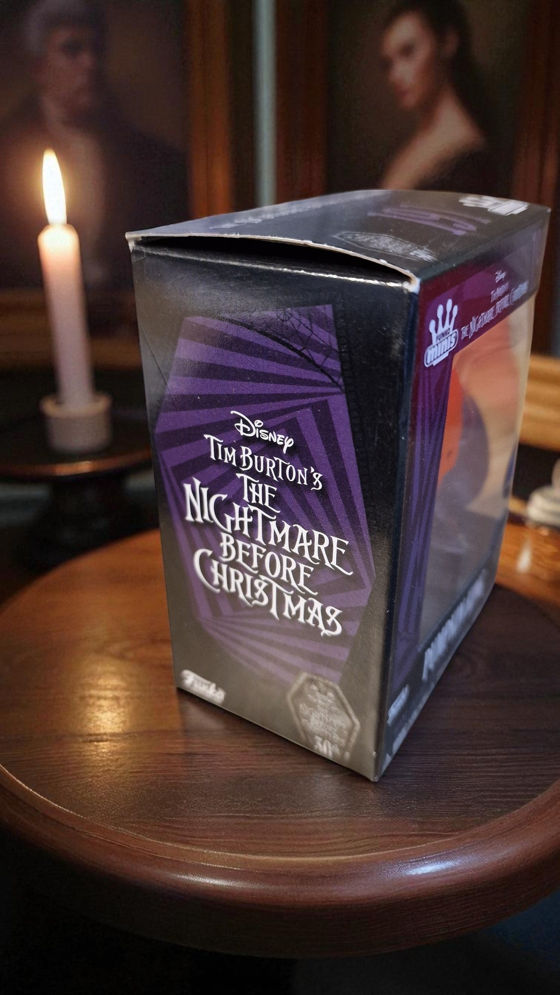 Box of Tim Burton's 'The Nightmare Before Christmas' on a wooden surface with a candle in the background.