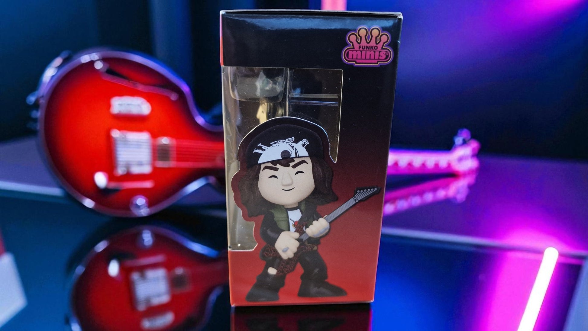 Boxed figurine with character design on a reflective surface with a guitar in the background