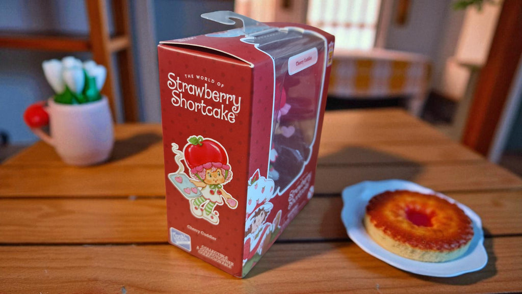 Strawberry Shortcake-themed product packaging on a wooden table with a cake.