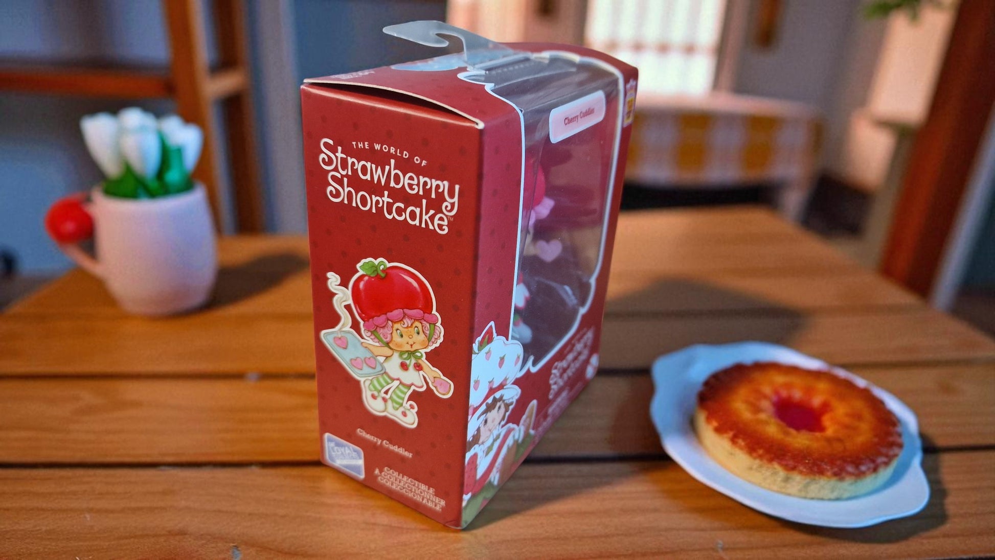 Strawberry Shortcake-themed product packaging on a wooden table with a cake.