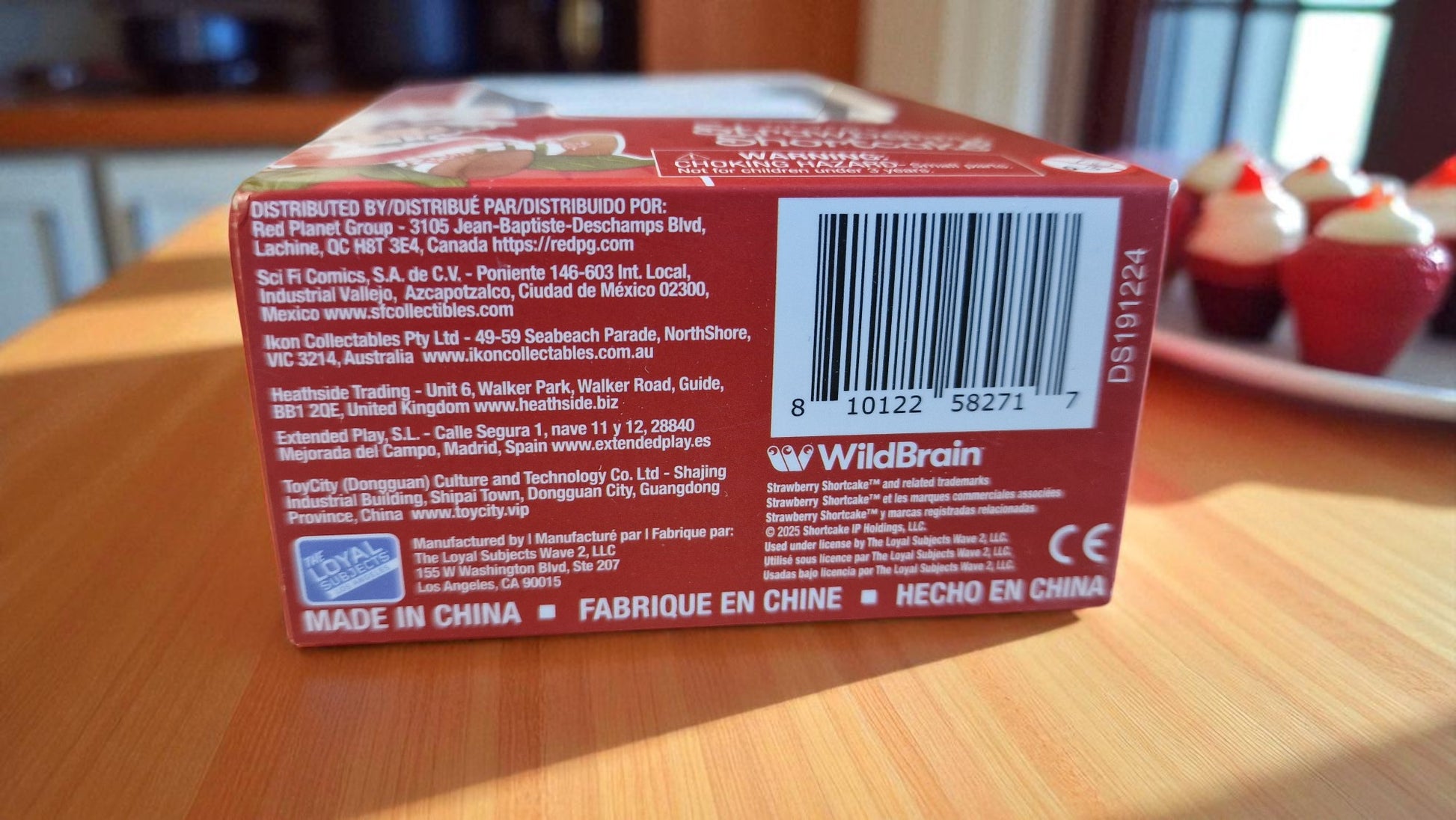 Back of a product box with a barcode and text, placed on a wooden surface.