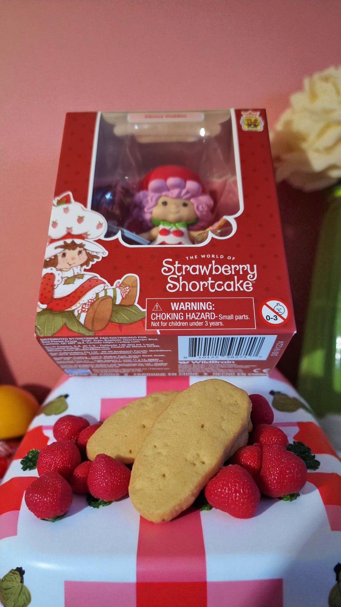 Strawberry Shortcake toy in packaging with cookies and strawberries on a checkered surface