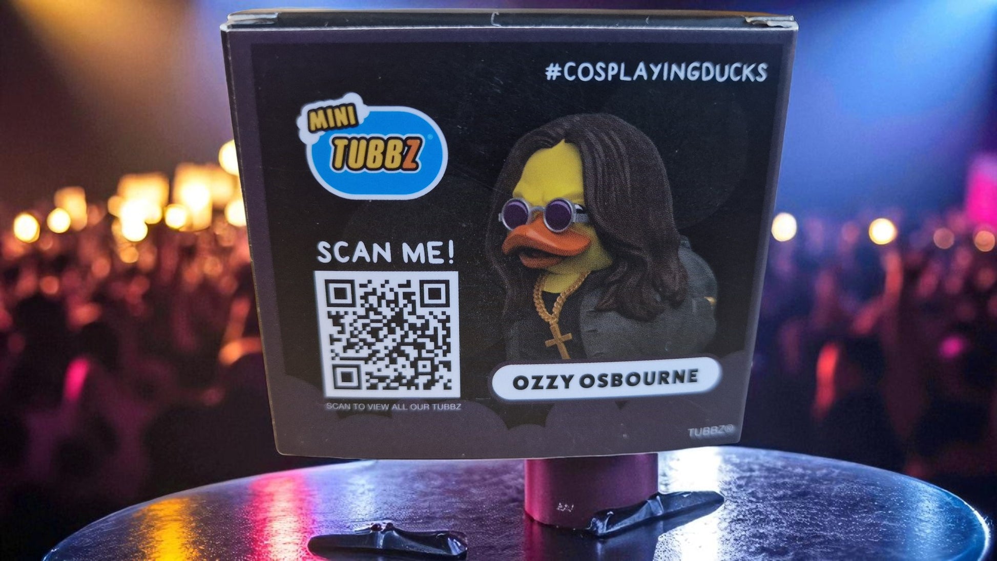 Mini Tubbz Ozzy Osbourne figure with a QR code on a stand in front of a crowd.