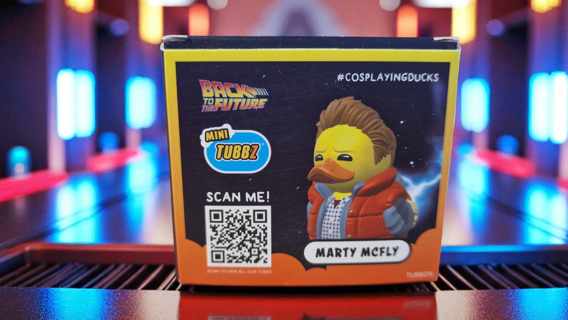 Miniature duck toy packaging with 'Back to the Future' theme and QR code on a blurred colorful background.