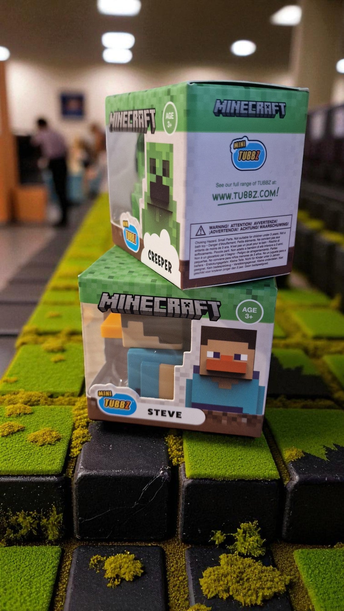 Two Minecraft figurine boxes on a textured surface with blurred indoor background