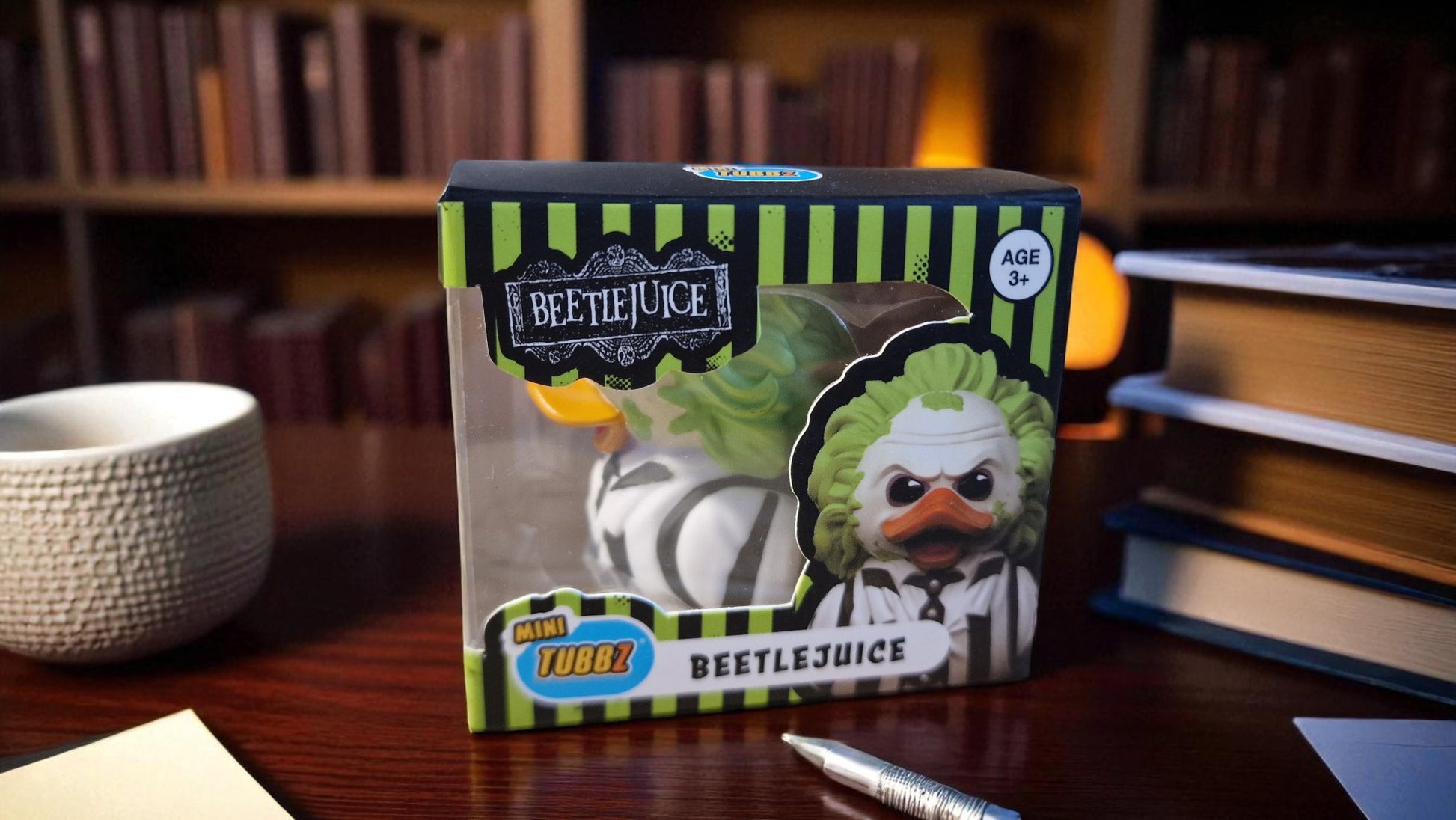 Beetlejuice toy figure in packaging on a desk with books and a bowl in the background