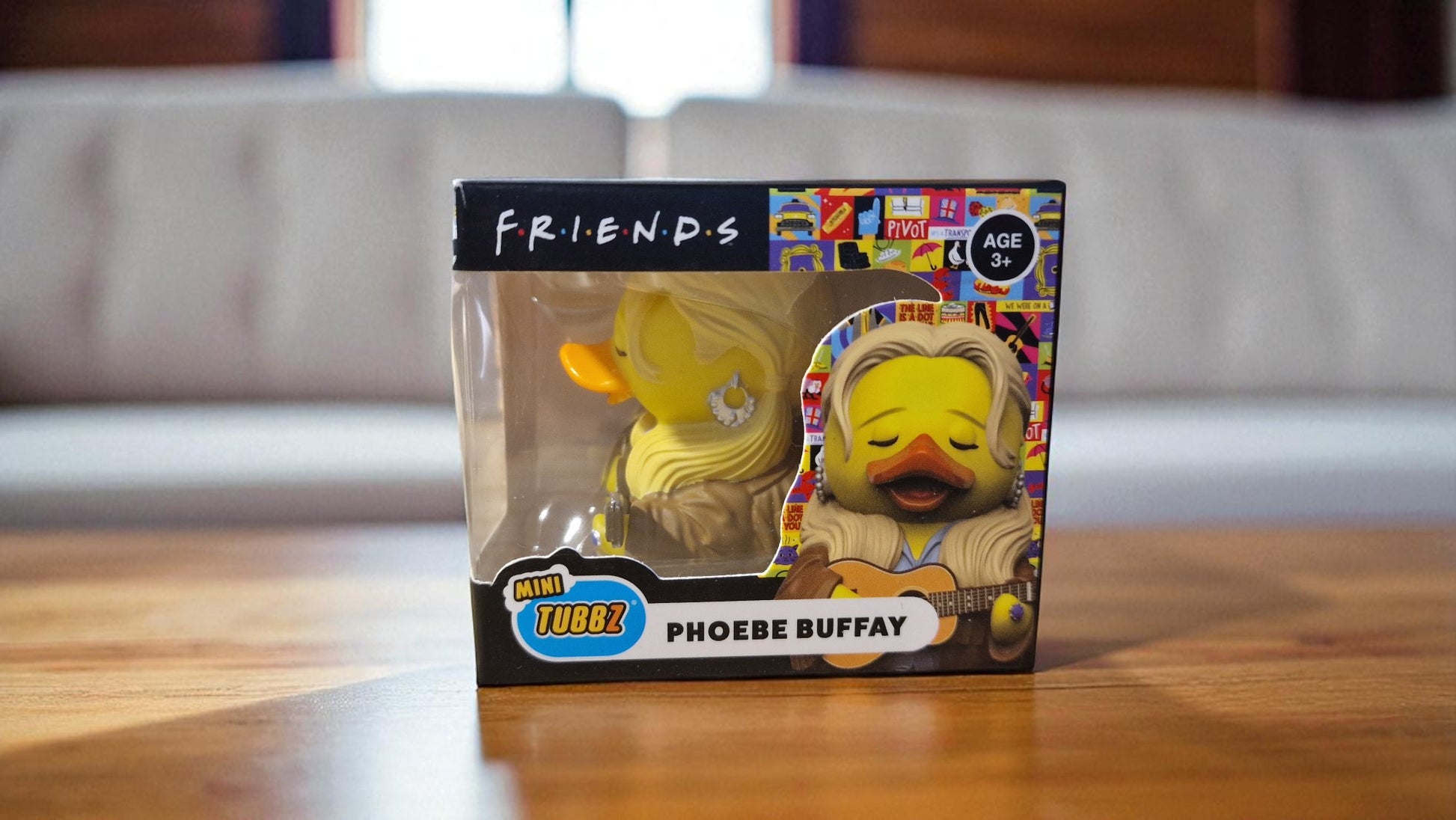 Packaged toy figure of a character from 'Friends' on a wooden surface.