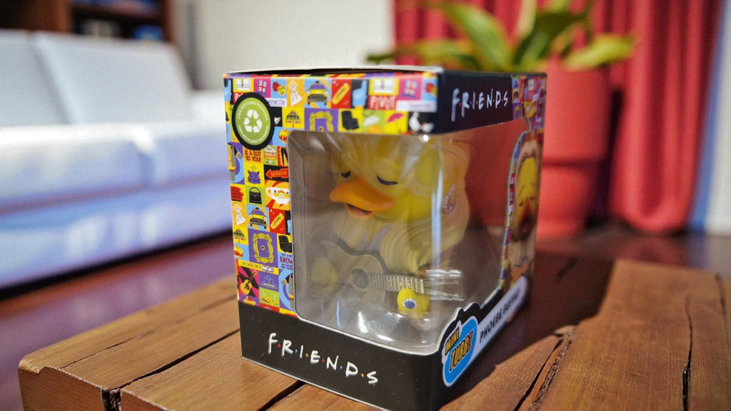 Rubber duck in a 'Friends' themed packaging on a wooden surface with a blurred background